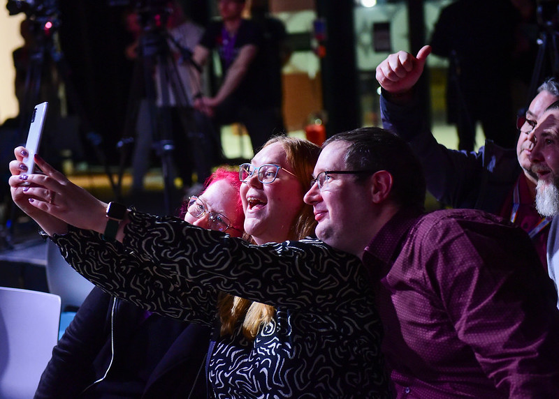 Three audience members taking a selfie on a mobile phone during the interval.